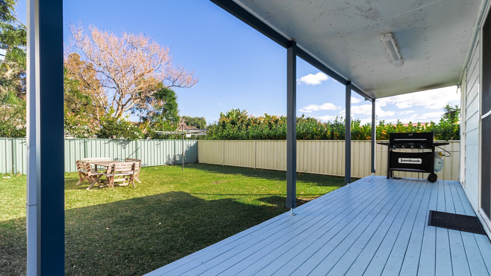 A covered patio with a grill, a wooden table, and a grassy yard.