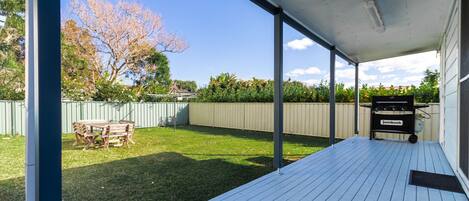 A covered patio with a grill, a wooden table, and a grassy yard.