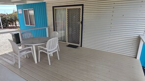 Ein überdachter Außenbereich mit Tisch und Stühlen, einer blauen Wand und einer Schiebetür.