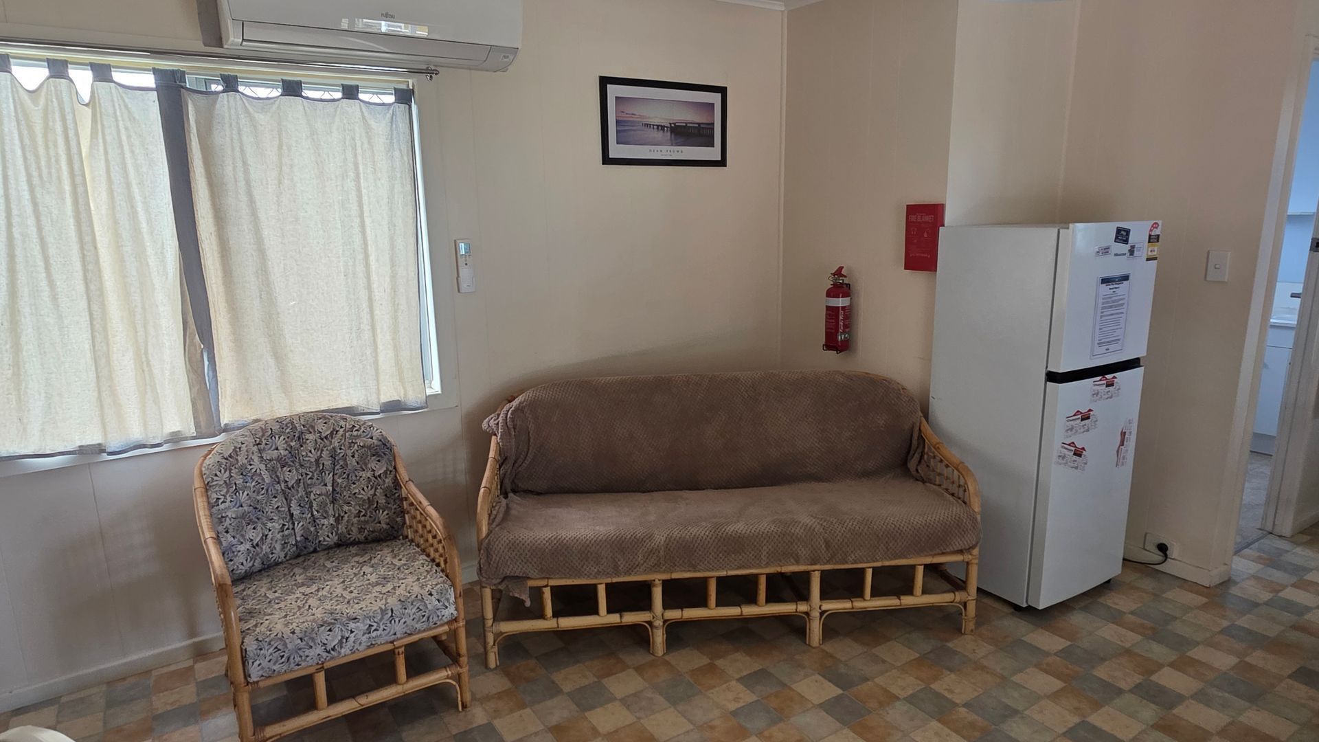 A room with a patterned chair, a brown sofa, a white refrigerator, and a window with curtains.