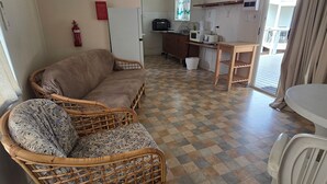 Habitació acollidora amb terra de pissos, un sofà de vimetes, una taula petita i una cuineta de fons.