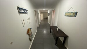 Un pasillo estrecho con una mesa de madera oscura y una pequeña escultura blanca encima. Hay varios carteles en las paredes, incluyendo uno que dice "Welcome".