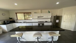 Una cocina moderna con armarios blancos, encimera negra y refrigerador de acero inoxidable. Hay tres taburetes de bar frente a la encimera.