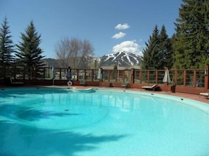 Ein klares, blaues Schwimmbecken mit Blick auf eine Berglandschaft, umgeben von Bäumen und einer Holzterrasse.