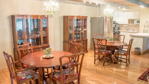 A dining area with a wooden table and chairs, a glass cabinet with glassware, and a kitchen in the background. - Atelier Condo 1107 - Charming Condo with Access to Sun Valley Resort Pool (Sun Valley)
