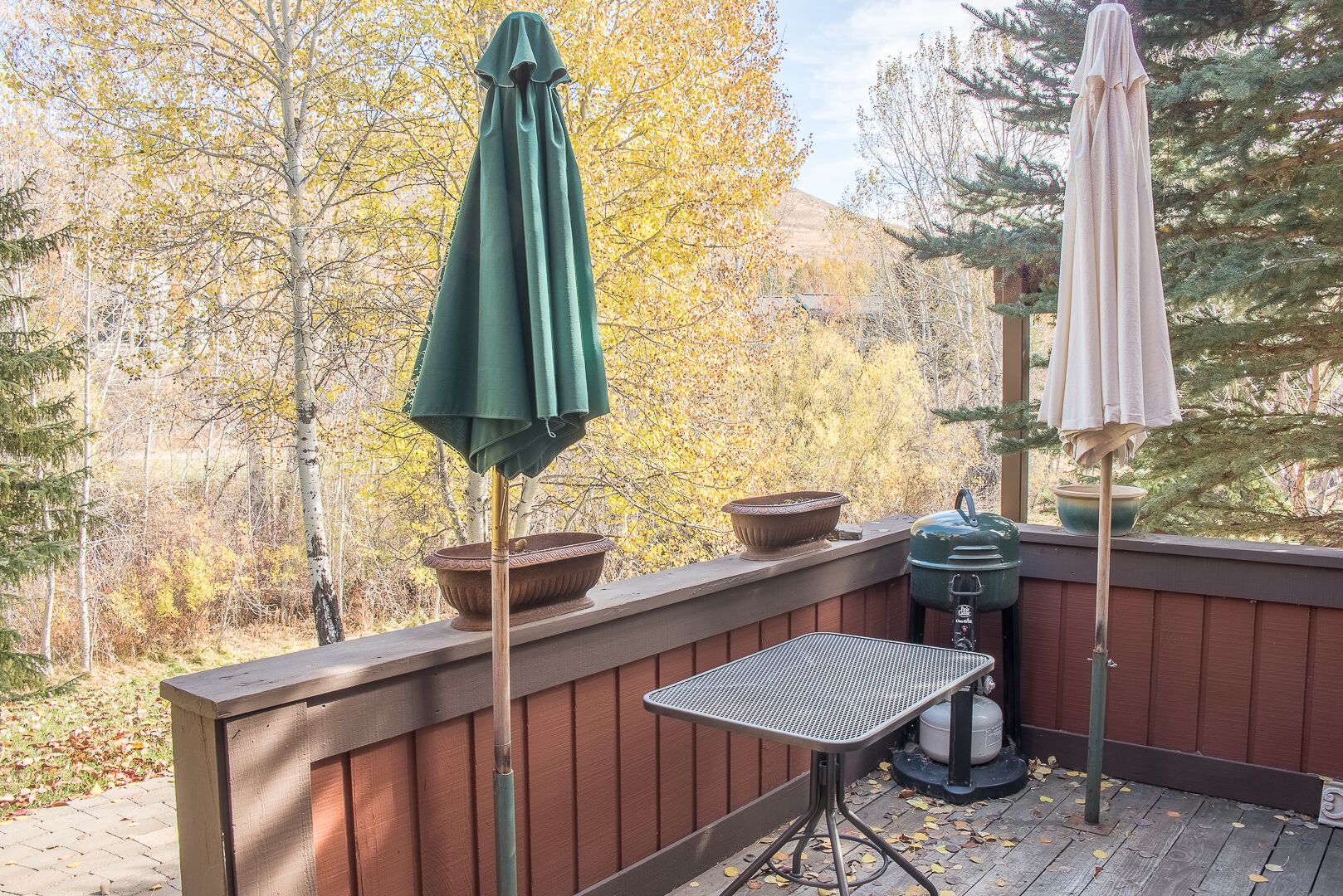 Eine Holzterrasse mit zwei Sonnenschirmen, einem Grill und einem Tisch.