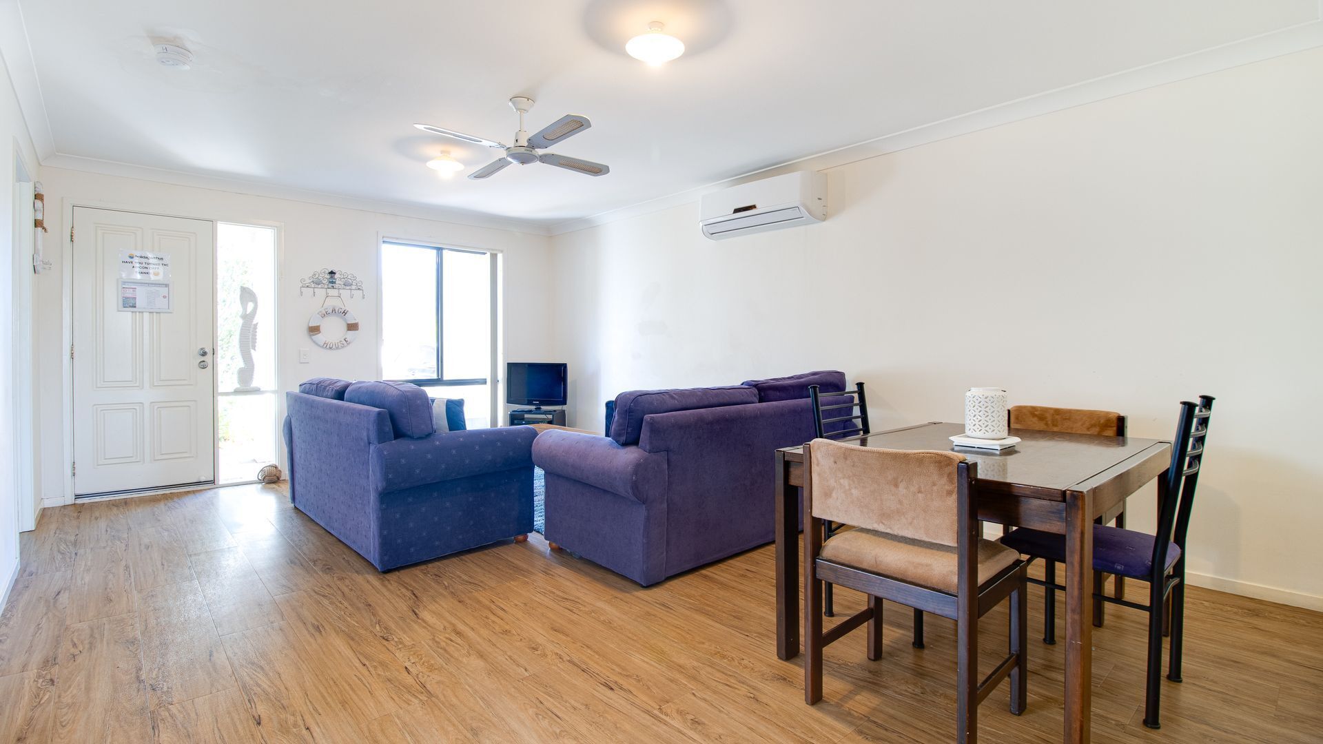 A modern living room with a sofa, a dining table with chairs, a ceiling fan, and a TV.