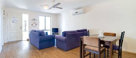 A modern living room with a sofa, a dining table with chairs, a ceiling fan, and a TV.