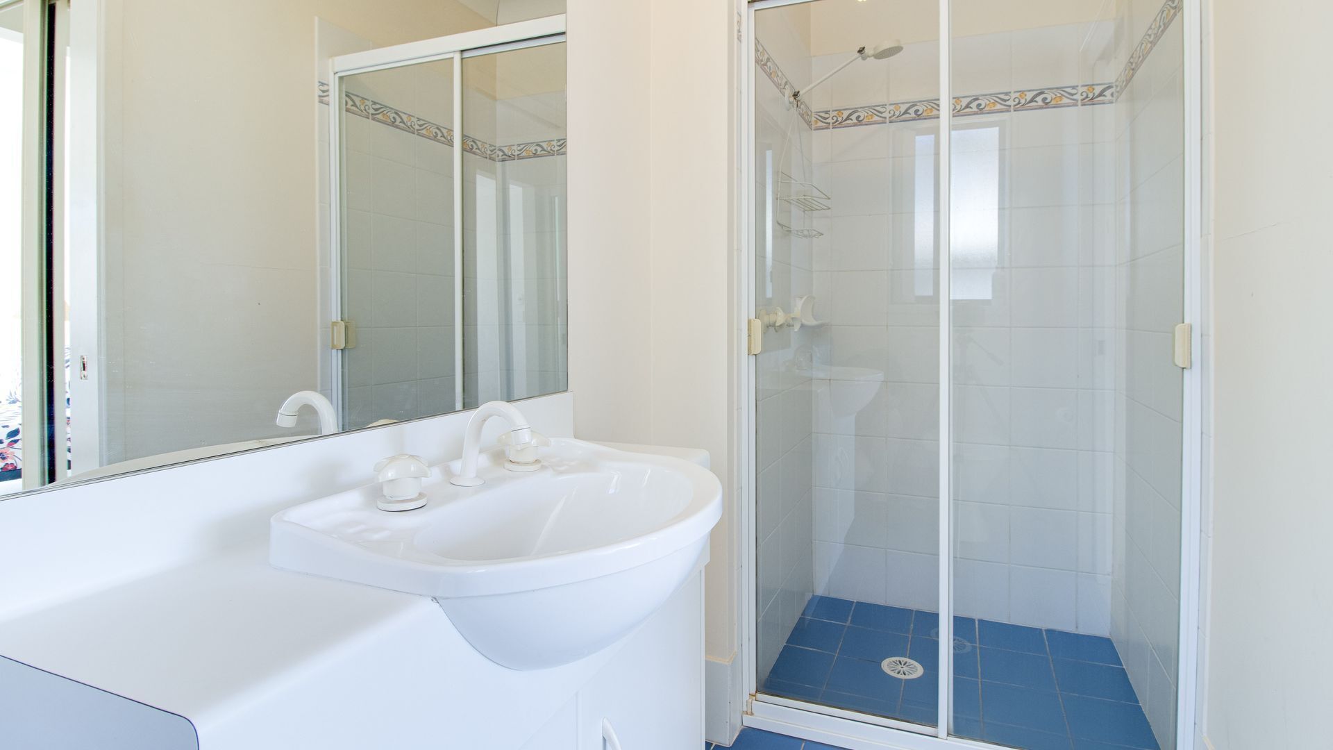Un baño con un lavabo blanco, un espejo y cabina de ducha con paredes de vidrio.