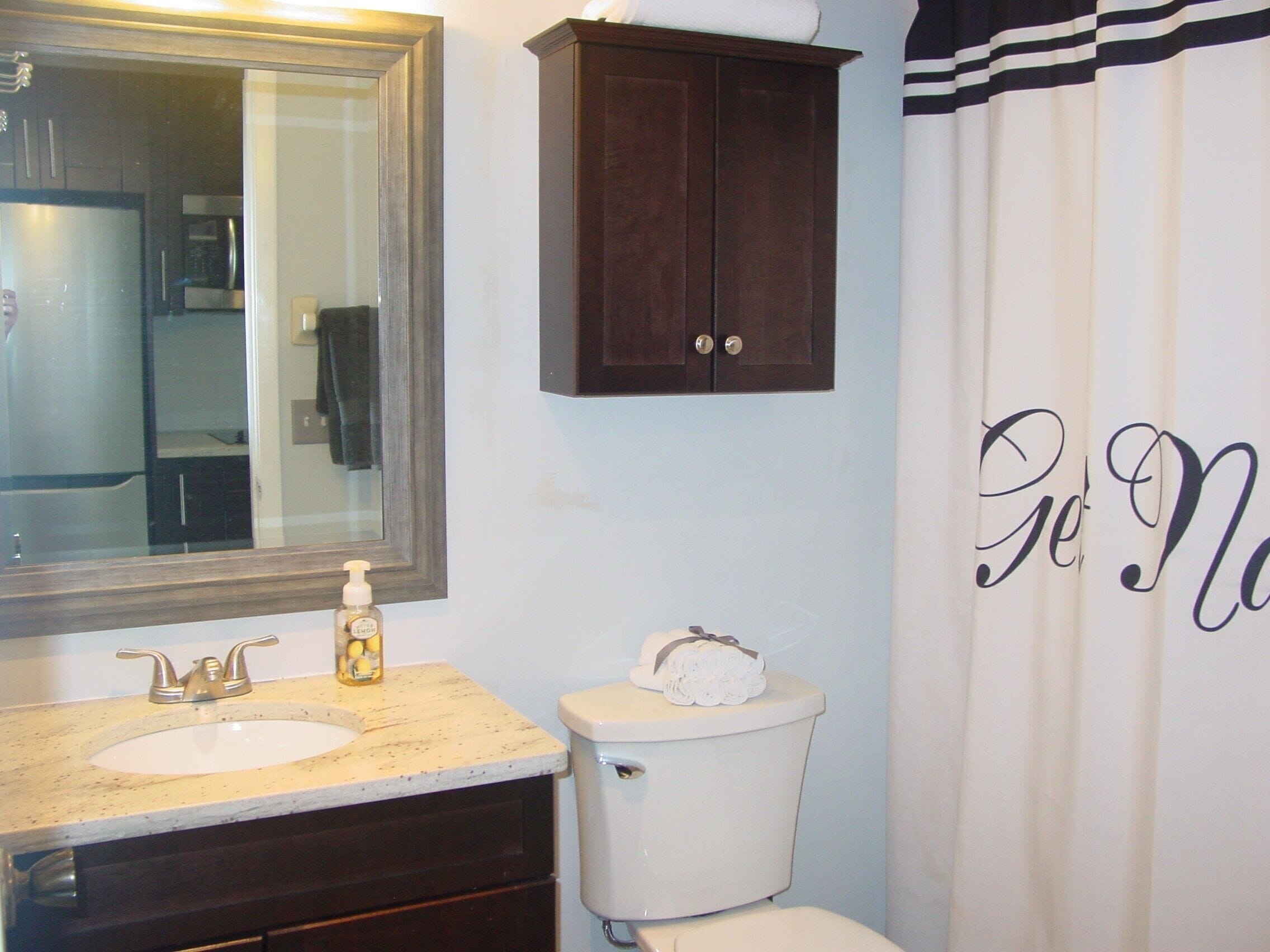 A bathroom with a sink, mirror, toilet, and a shower curtain with the text "Go Now".