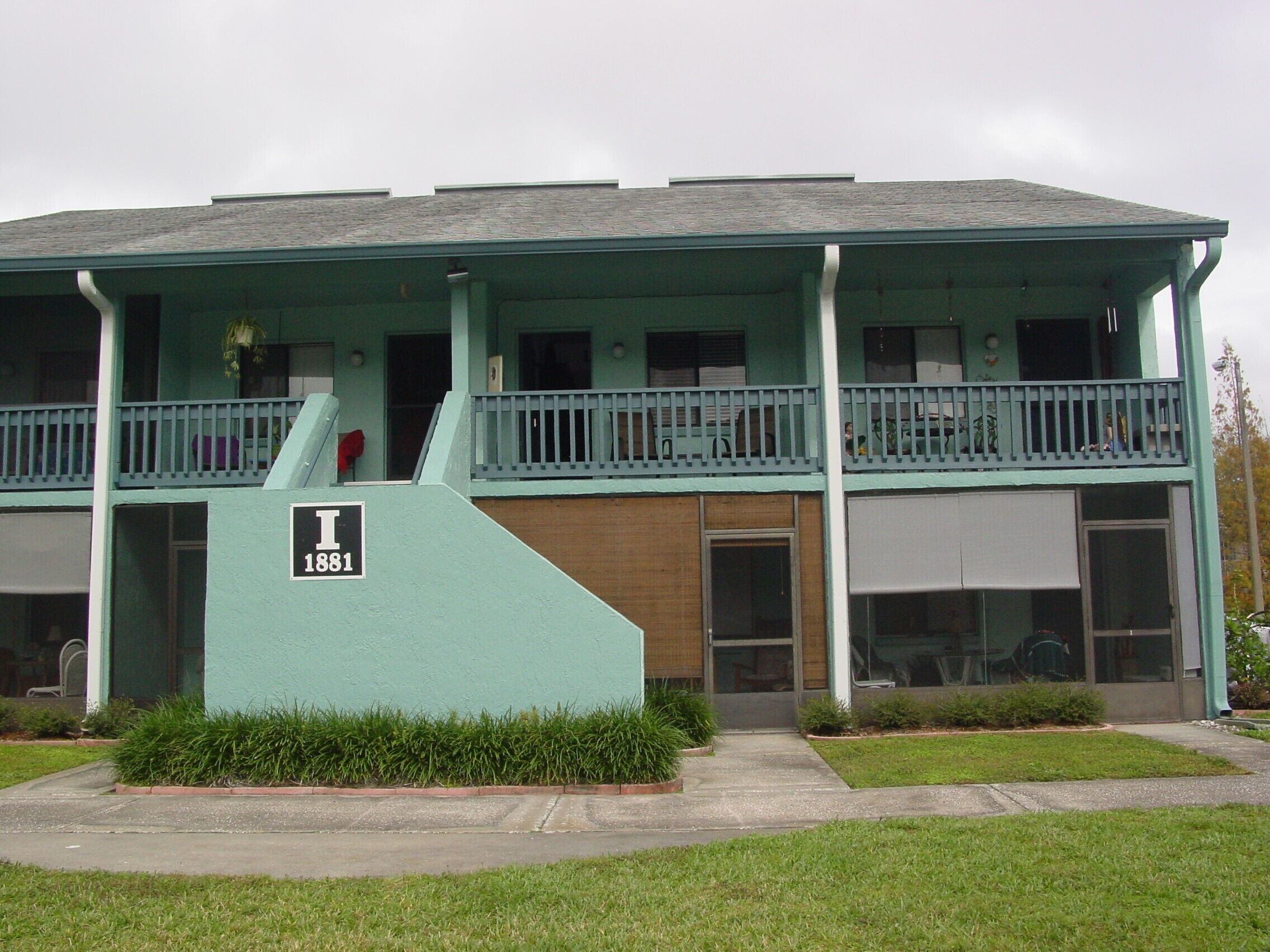A two-story building with a flat roof, a balcony on the upper floor, and a sign indicating the address.