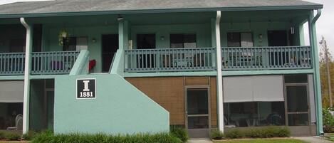 A two-story building with a flat roof, a balcony on the upper floor, and a sign indicating the address.