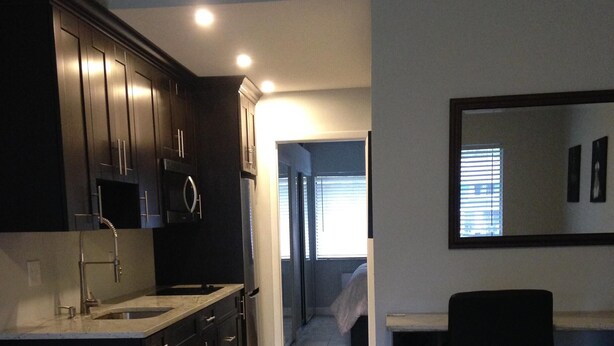 A modern kitchen with dark cabinetry, a stainless steel sink, and a bar area with a stool.