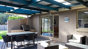 An outdoor patio with a grill, wicker furniture, and a sliding glass door leading to a covered area.