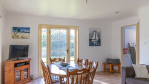 A dining area with a table and chairs, a television on a cabinet, and artwork on the walls.