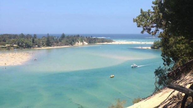 A coastal landscape with clear turquoise waters, sandy beaches, and a boat in the distance.