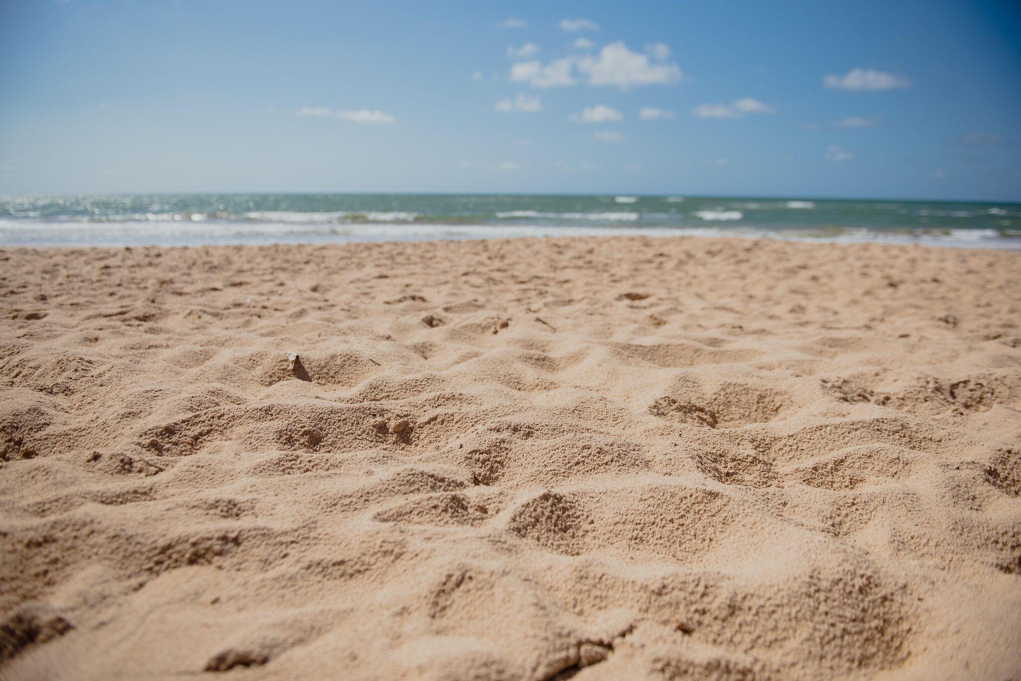 Ein sandiger Strand mit Fußabdrücken, die ins Wasser führen.