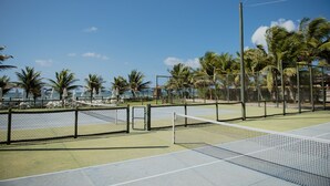 En tennisbane med net, omgivet af palmer og parasoller.