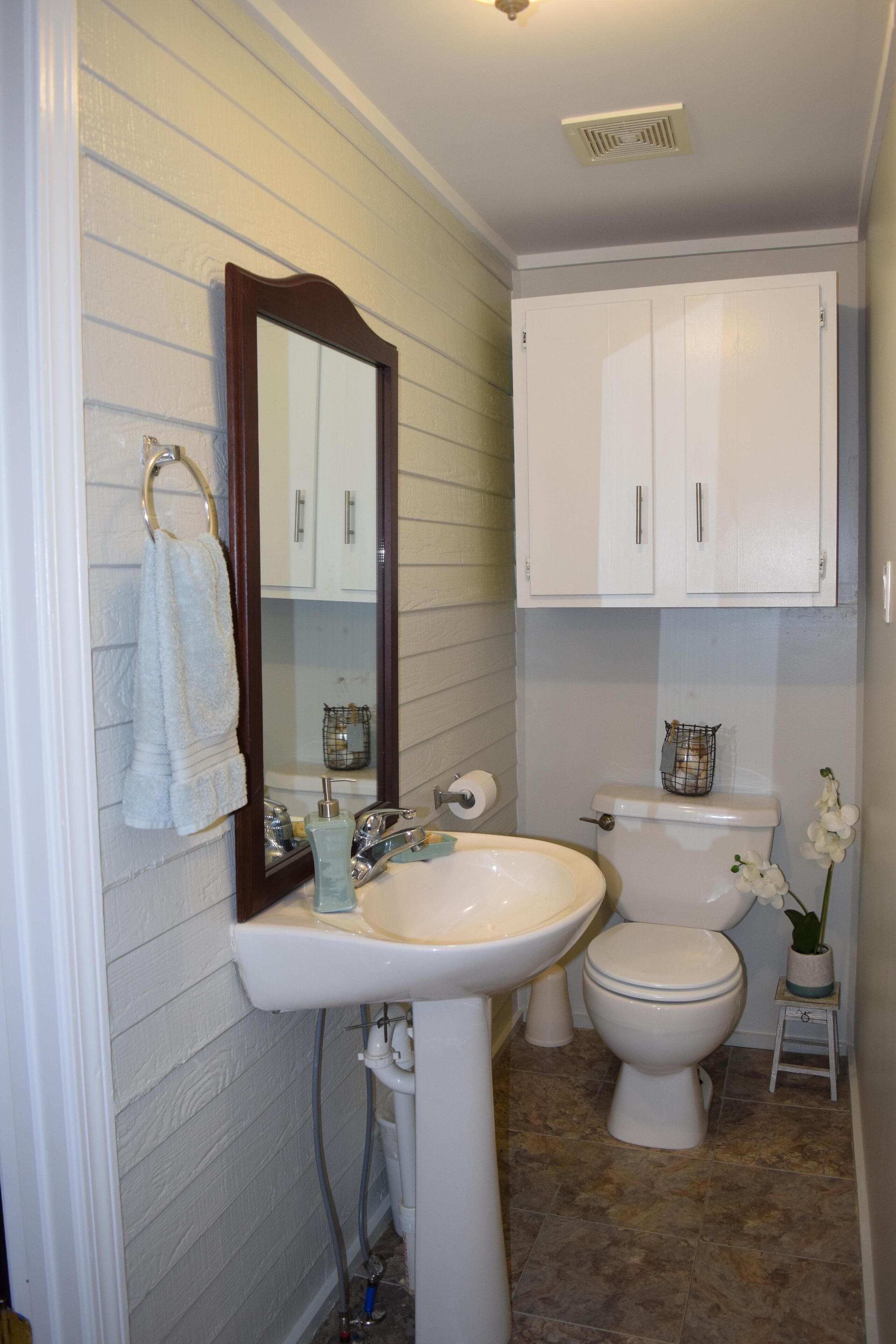 A bathroom with a sink, mirror, toilet, and cabinets.