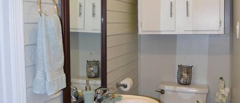 A bathroom with a sink, mirror, toilet, and cabinets.