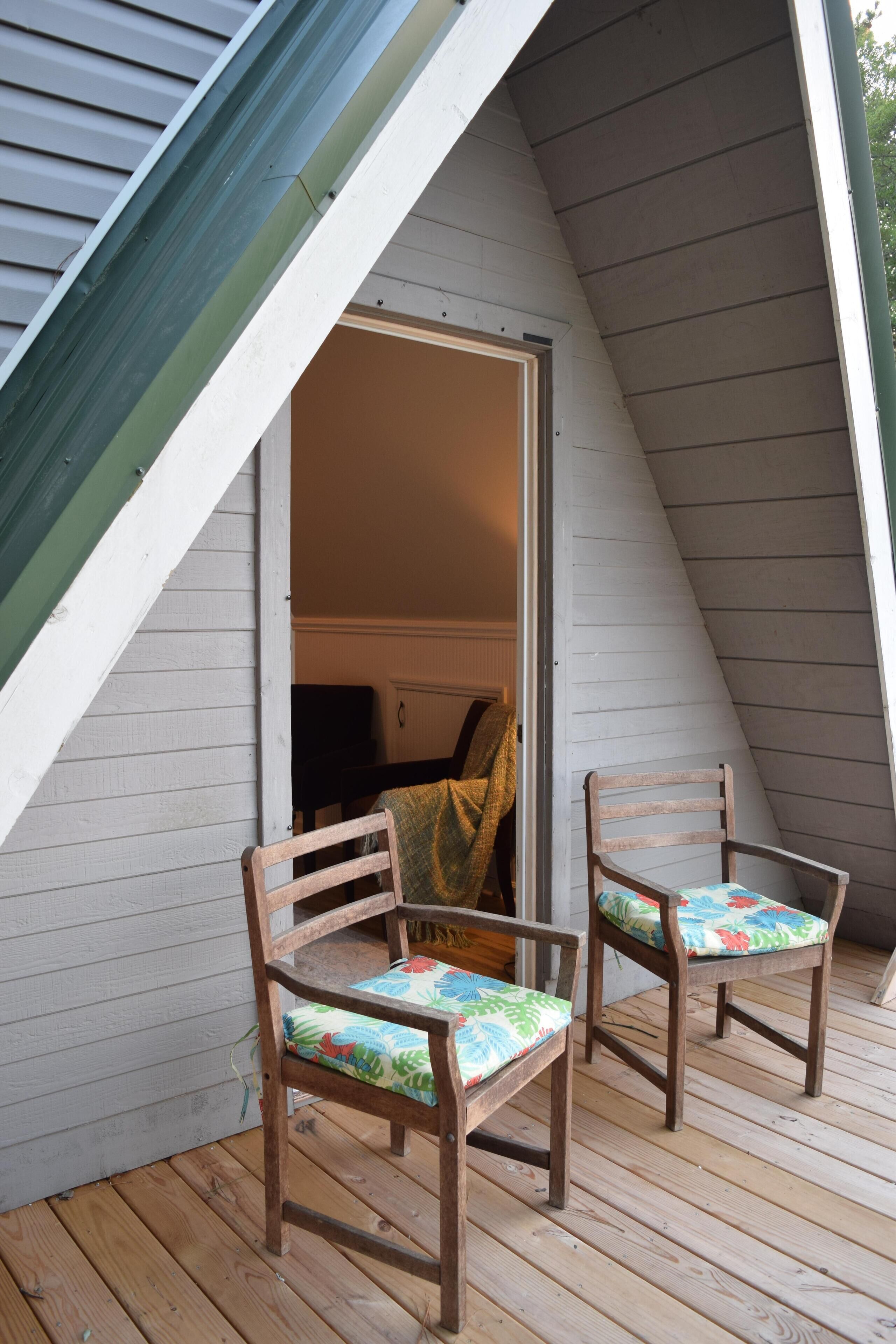 Eine Holzterrasse mit zwei Stühlen und einer Tür zu einem Innenraum.