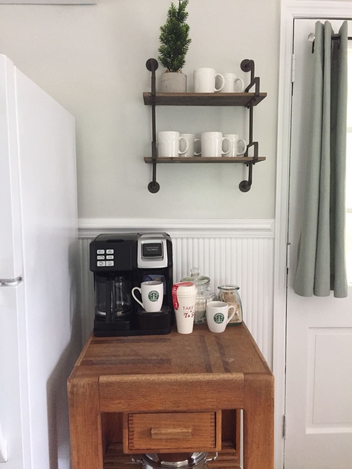 Un coin cuisine équipé d’une machine à café, de tasses et d’une petite étagère sur laquelle se trouvent une plante et des verres.