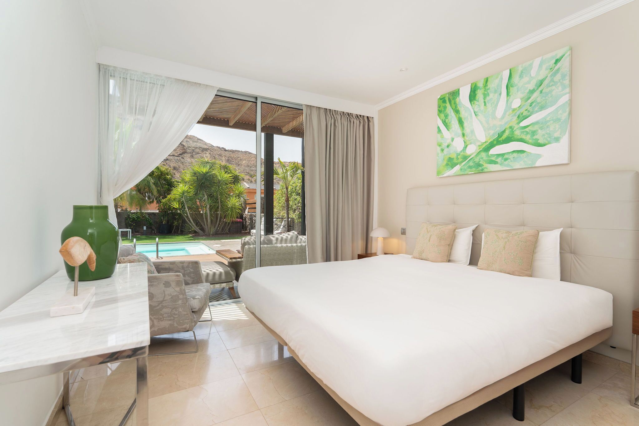 A hotel room with a large bed, a desk, and a view of a pool and mountains.