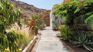 A pathway leading to a building with a mountain backdrop, surrounded by various plants and a stone-tiled walkway. - LUXURY PROPERTY, PRIVATE HEATED POOL, FREE FIBER WIFI (Mogán)