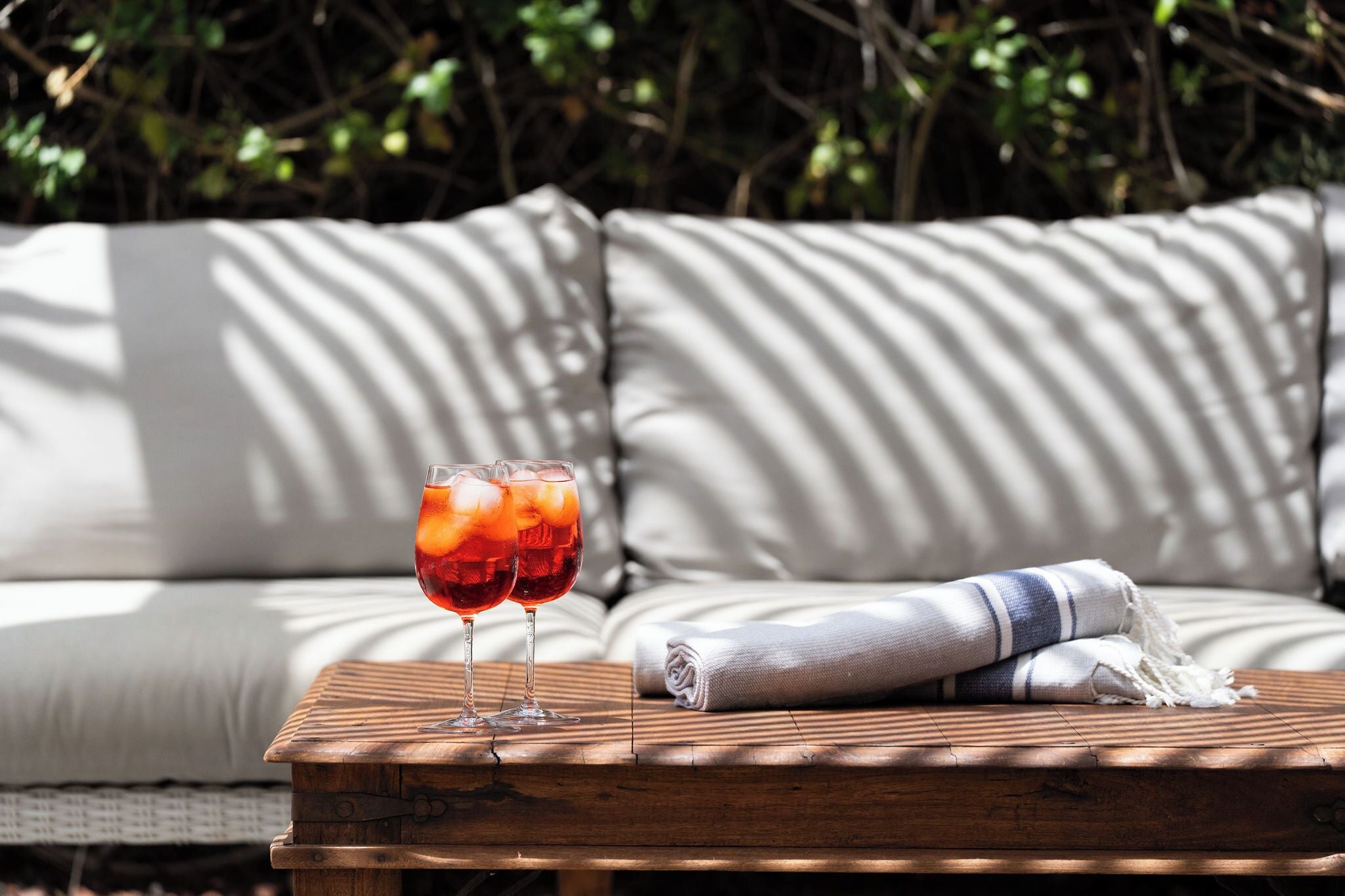 A wooden table with two glasses of red drink, a folded towel, and a sofa with striped cushions.
