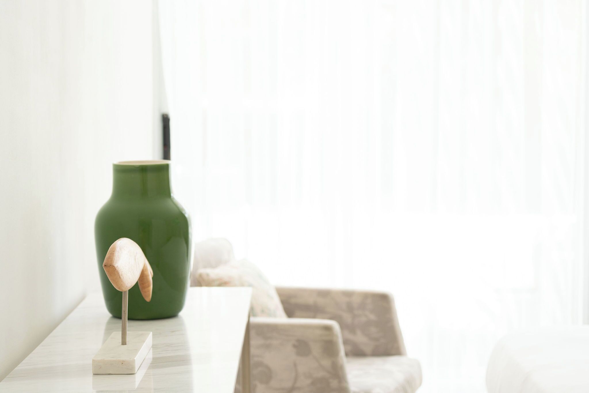 A green vase on a white surface with a wooden object on a stand.