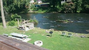 Zona de picnic a la orilla del río, con bancos y un hogar para fuego.