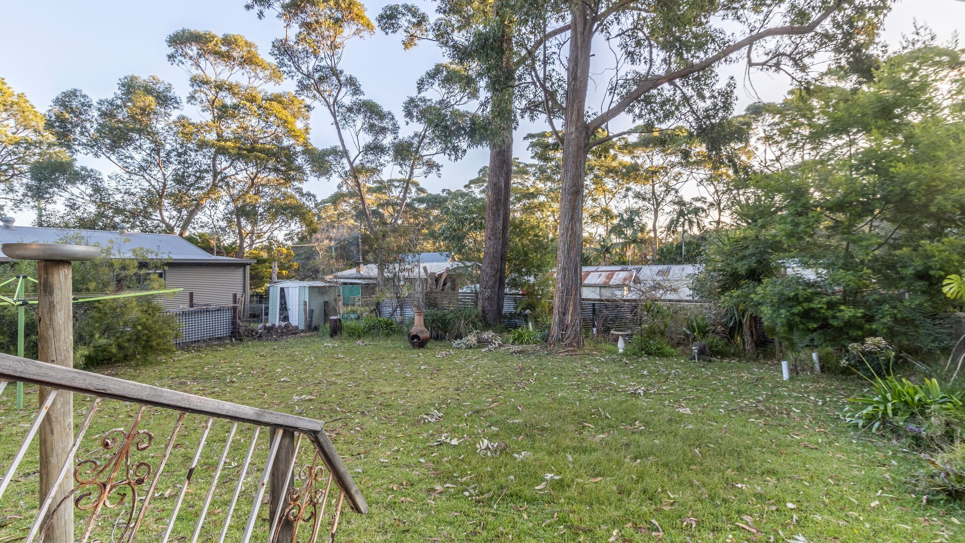 A residential backyard with a wooden deck, a small shed, and a large tree.