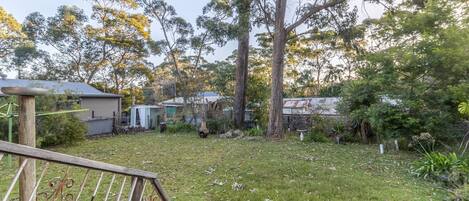 A residential backyard with a wooden deck, a small shed, and a large tree.