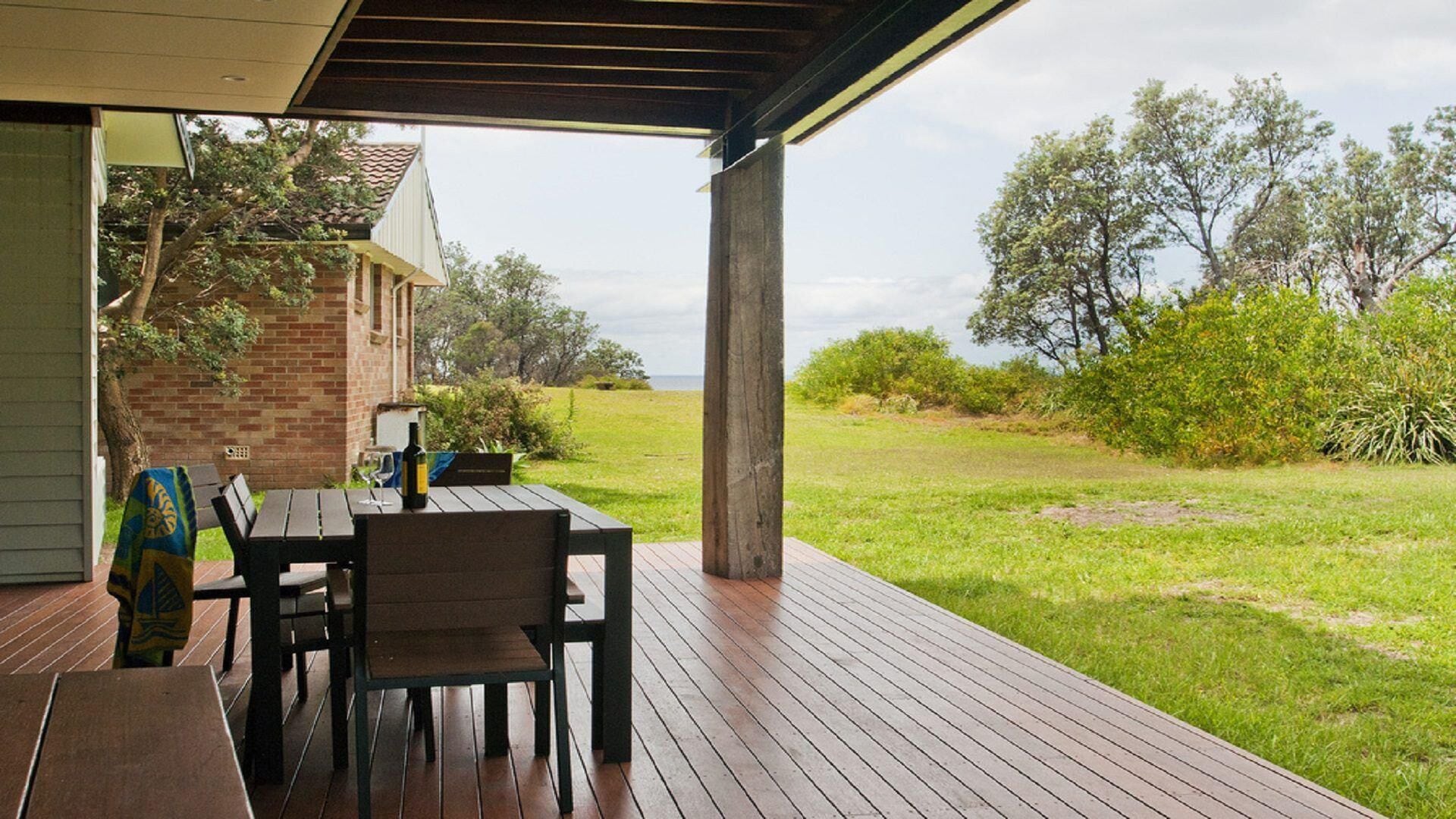 An outdoor patio with a wooden deck, a table with chairs, and a bottle of wine.