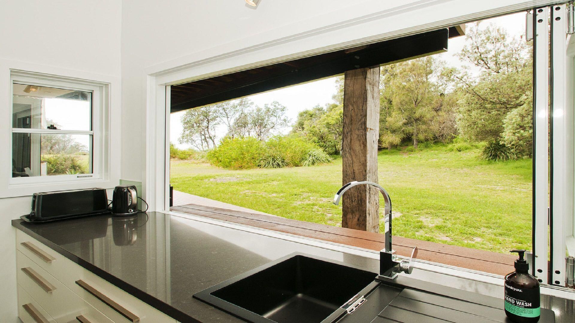 A kitchen with a black countertop, a sink, and a window overlooking a grassy area.