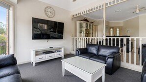 A living room with a flat-screen TV, a glass coffee table, a leather sofa, a white entertainment unit, and a white railing. - Cormorant Waterfront Home (Sussex Inlet)