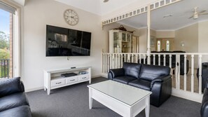 A living room with a flat-screen TV, a glass coffee table, a leather sofa, a white entertainment unit, and a white railing. - Cormorant Waterfront Home (Sussex Inlet)