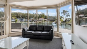 Una sala de estar moderna con un sofá de cuero negro, una mesa de centro de vidrio y vistas a un lago y edificios.