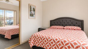 A bedroom with a bed, a nightstand, a mirror, and a framed picture on the wall. - Cormorant Waterfront Home (Sussex Inlet)