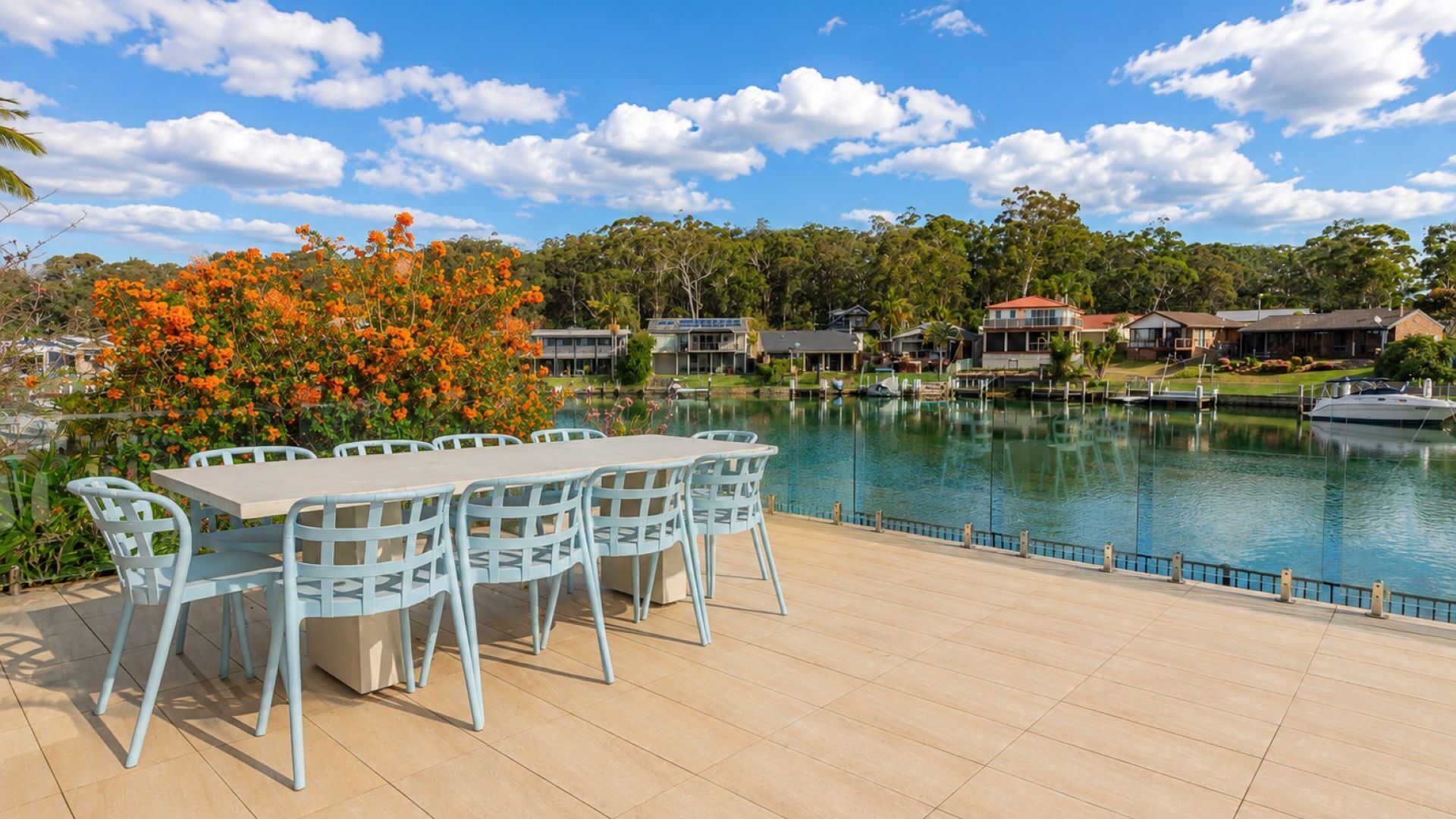 A lakeside patio with a dining table and chairs, surrounded by a swimming pool and residential buildings.