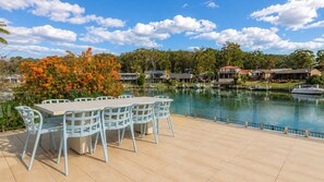 Un patio junto al lago con una mesa y sillas, rodeado por una piscina y edificios residenciales.