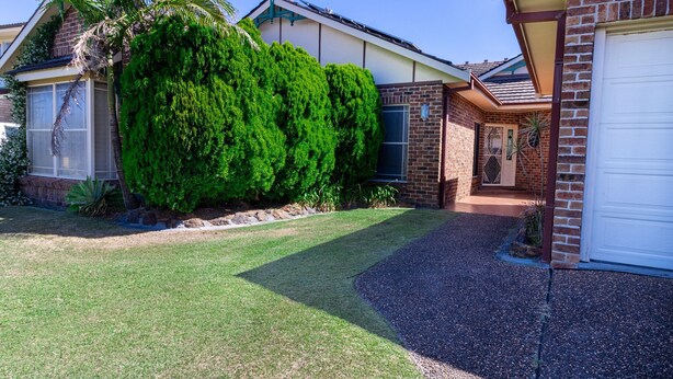 A residential property with a well-maintained lawn, a large coniferous tree, and a brick exterior. - Cormorant Waterfront Home (Sussex Inlet)