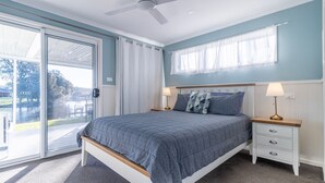 Una camera da letto con un letto, comodini, una ventola a soffitto e vista su un lago.