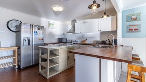 Una cucina moderna con mobili bianchi, un'isola centrale, elettrodomestici in acciaio inossidabile e illuminazione a sospensione.