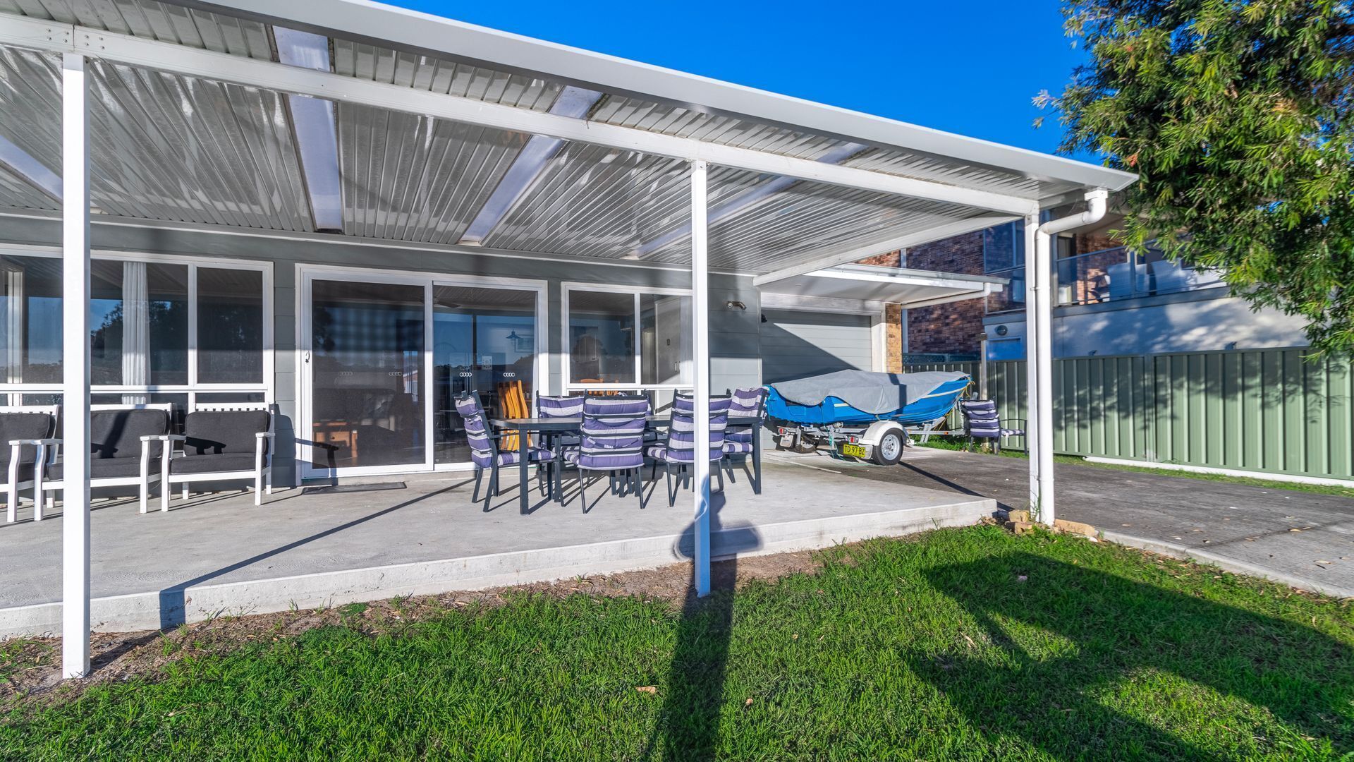A covered outdoor area with a table and chairs, a covered boat, and a garage door.