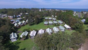 An aerial view of a campground with multiple cabins, surrounded by dense trees and a clear view of the ocean. - Sea Shell Chalet @ Berrara Chalet (Berrara)