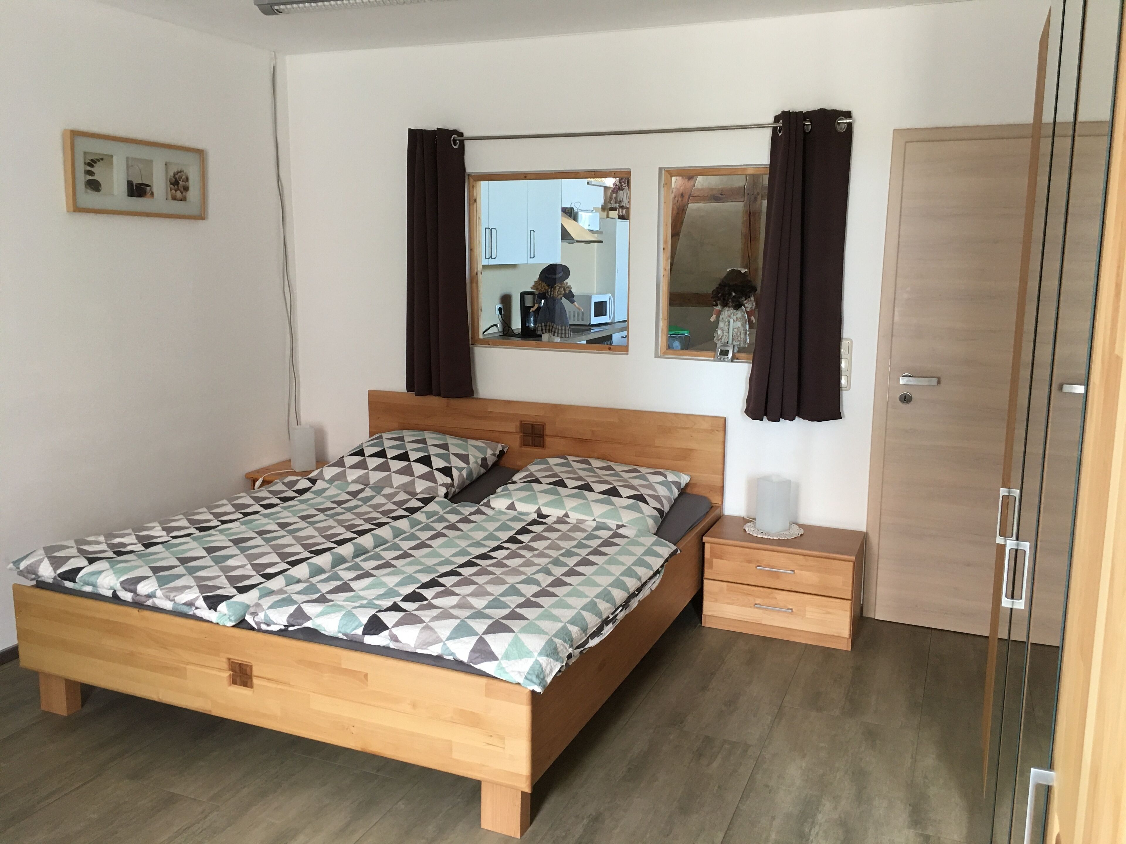 A bedroom with a wooden bed, a bedside table with a lamp, a wardrobe, and a mirror on the wall.
