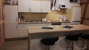 A compact kitchen with white cabinets, a stainless steel range hood, a microwave, and a refrigerator. There are three black bar stools at the counter. - Quiet large apartment between Nemitzer Heide and Elbtalaue (Trebel)