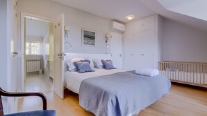 Une chambre à coucher comprenant un lit, un berceau, une chaise, un radiateur et une porte donnant sur une autre pièce.