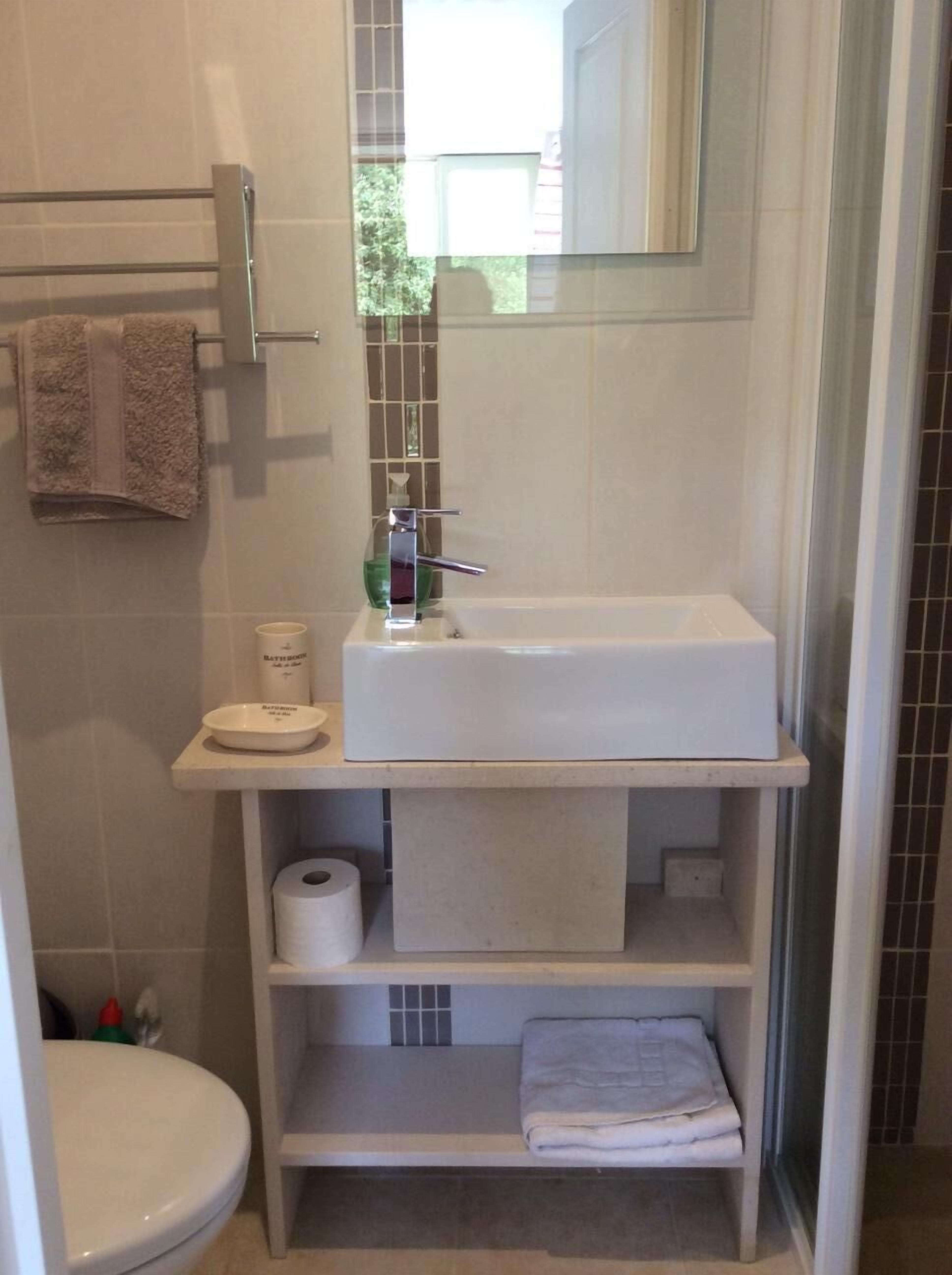 A bathroom with a white sink, a toilet, a towel rack, and a shelf with a towel and toilet paper.